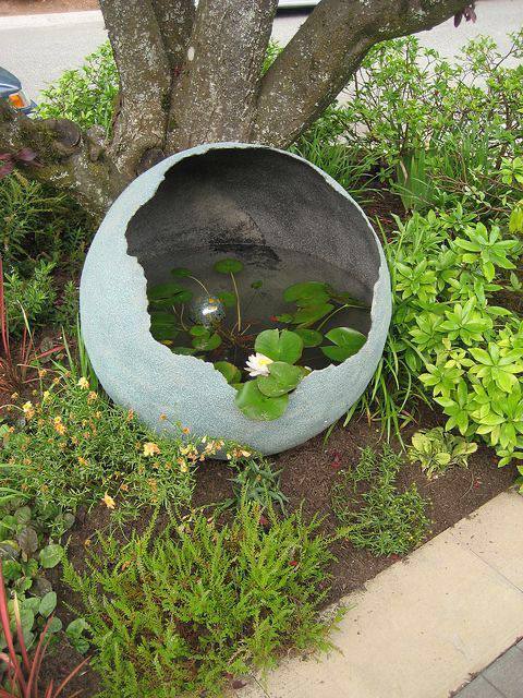 Image 2: broken concrete sphere water feature with aquatic plants